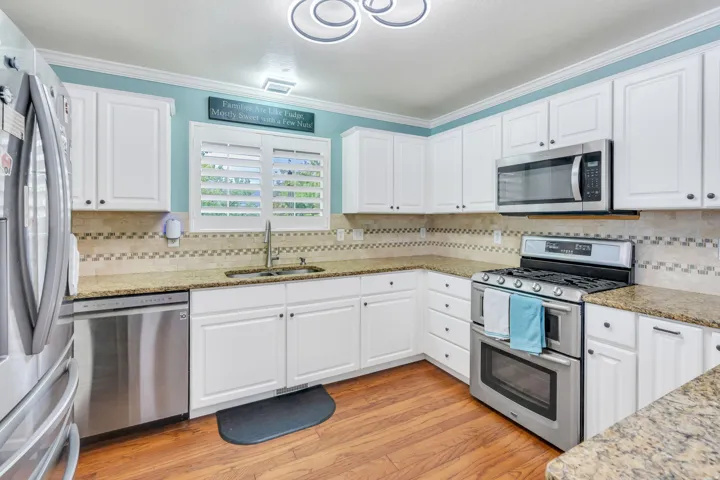 White cabinetry, granite-finish countertops, stainless steel appliances, wood-finish flooring, and a patterned tile backsplash