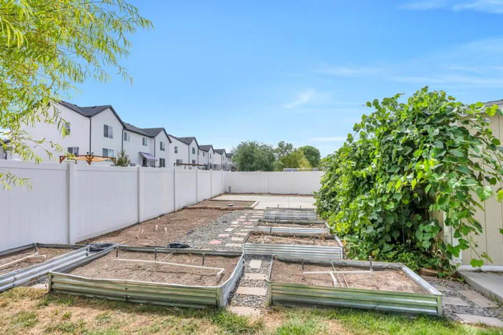 Private backyard featuring a white vinyl fence, multiple raised garden beds, and a paved patio area