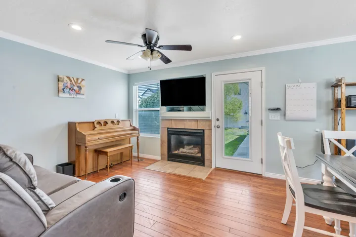 Wood-finish flooring, ceiling fan, recessed lighting, and a fireplace with a tile surround