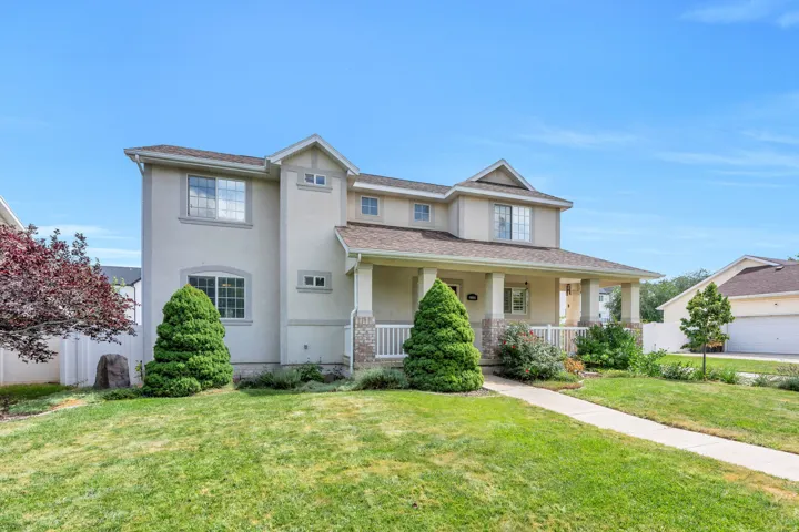Two-story stucco exterior with gabled roof lines, covered front porch, and mature front yard landscaping