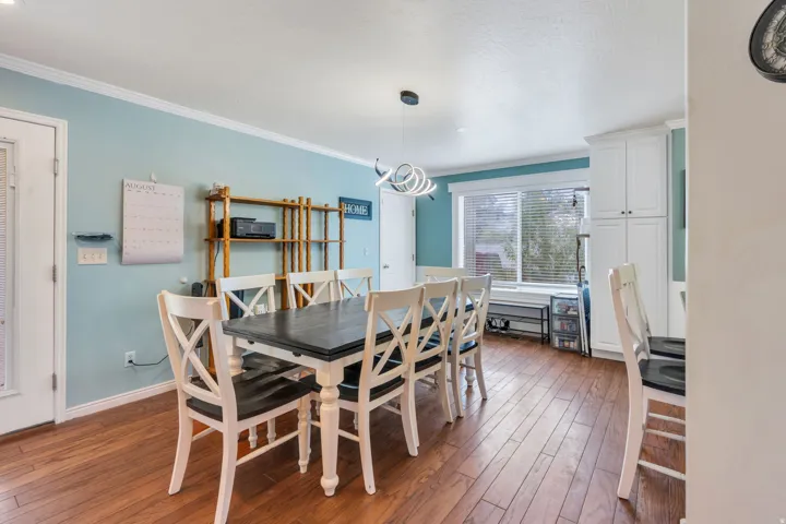 Wood-finish flooring, white crown molding, light blue wall paneling, built-in white cabinetry, and a contemporary light fixture