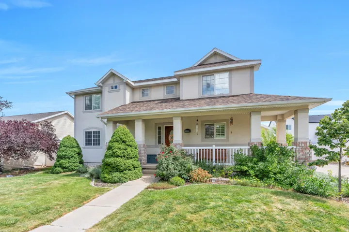 Two-story stucco exterior with dormer windows, covered front porch with white railing, stone column accents, and a concrete walkway