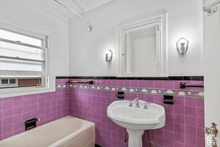 Pedestal sink with chrome fixtures, tiled walls featuring decorative trim, wall-mounted sconce lighting, and a built-in medicine cabinet