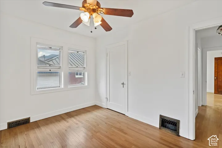 Hardwood flooring, painted white walls, ceiling fan with integrated lighting, and multiple windows