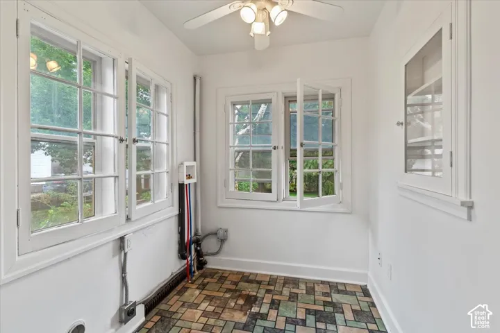Room featuring multiple casement windows, a ceiling fan with light fixture, built-in wall cabinetry, and patterned floor tile