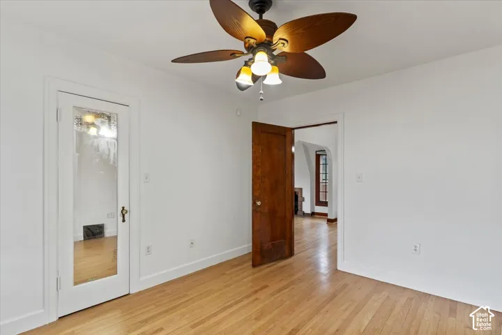 Light wood-finish flooring, white painted walls, and a ceiling-mounted fan with integrated lighting