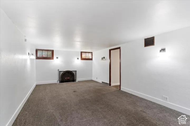 Carpeted room featuring a fireplace with screen, two wall-mounted light fixtures, and two windows with wood trim
