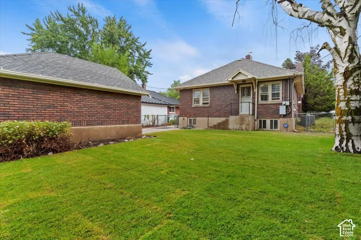Brick exterior home with a gabled roofline, mature trees, a detached garage, and a spacious lawn