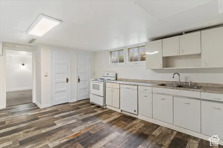 Kitchen featuring wood-finish flooring, white cabinetry, a double basin sink, and white appliances