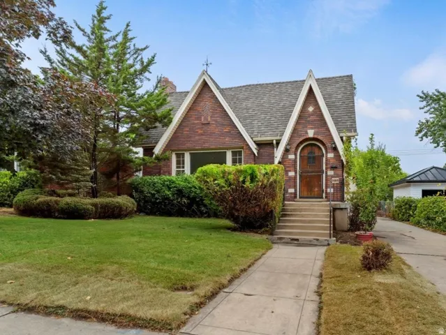 Brick exterior with gabled roof lines, arched entry door, mature trees, and a paved driveway