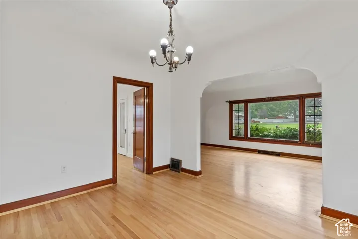 Hardwood flooring, arched doorway, wood trim, white walls, and a multi-light chandelier