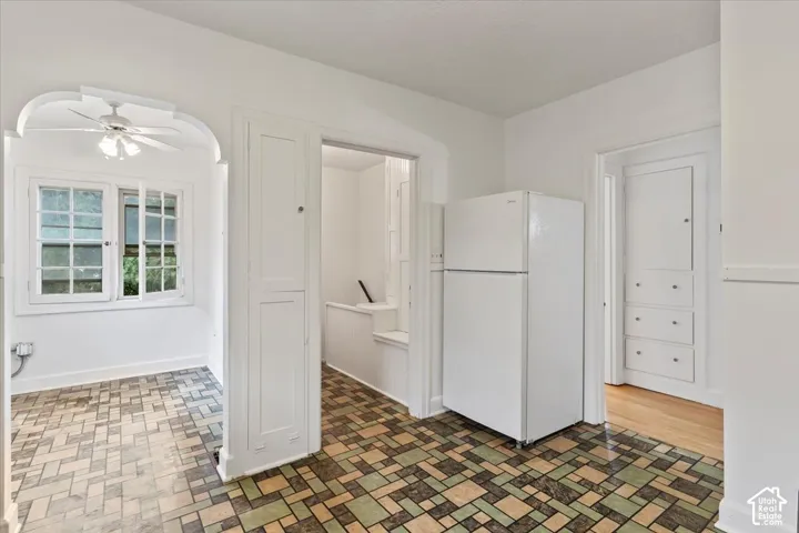 Patterned tile flooring, built-in storage cabinetry, white walls, white refrigerator, and a ceiling fan