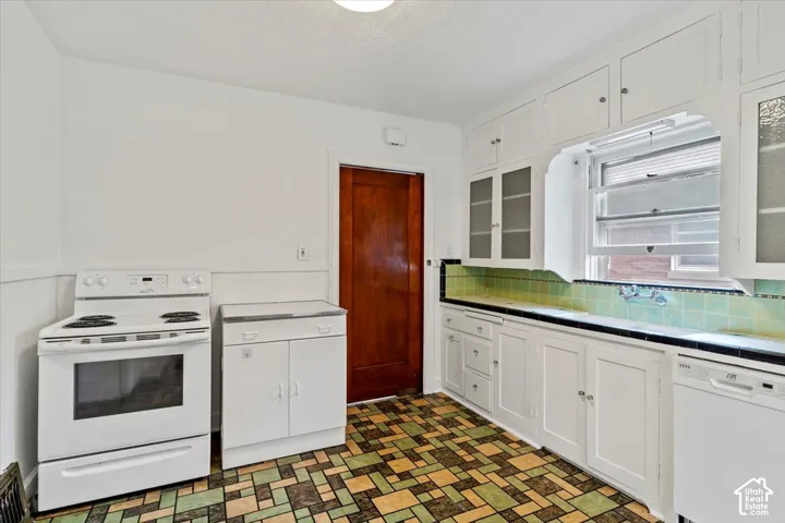 White cabinetry with glass-front uppers, patterned tile flooring, and a tiled backsplash