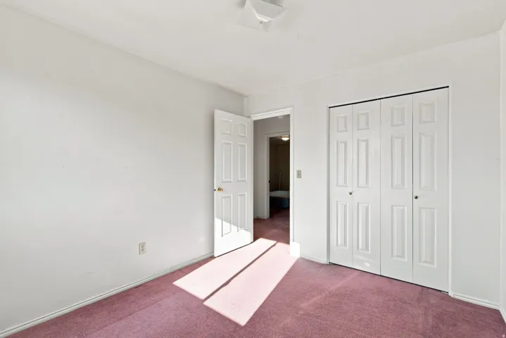 Bedroom with plush pink carpet, white walls, and bi-fold closet doors