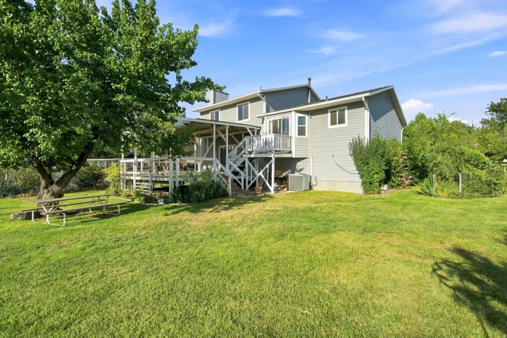 Expansive grassy yard with mature trees, multi-level wooden deck, and a gray siding exterior