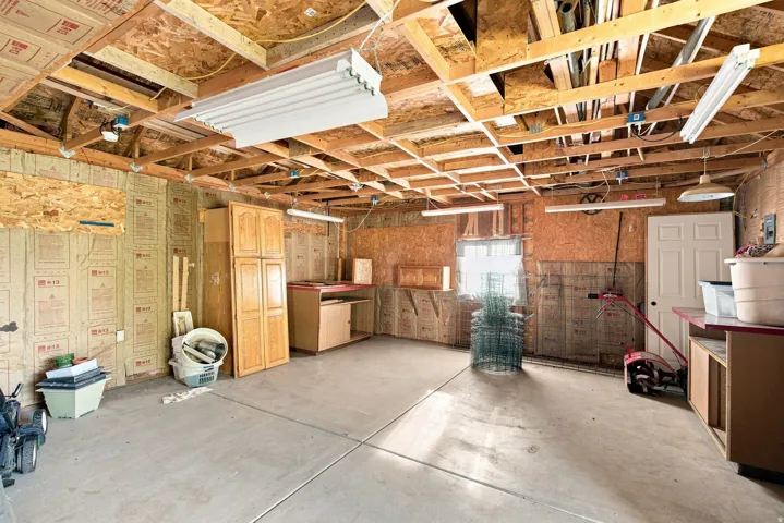 Spacious utility area featuring exposed wood framing, concrete flooring, built-in cabinetry, and overhead fluorescent lighting