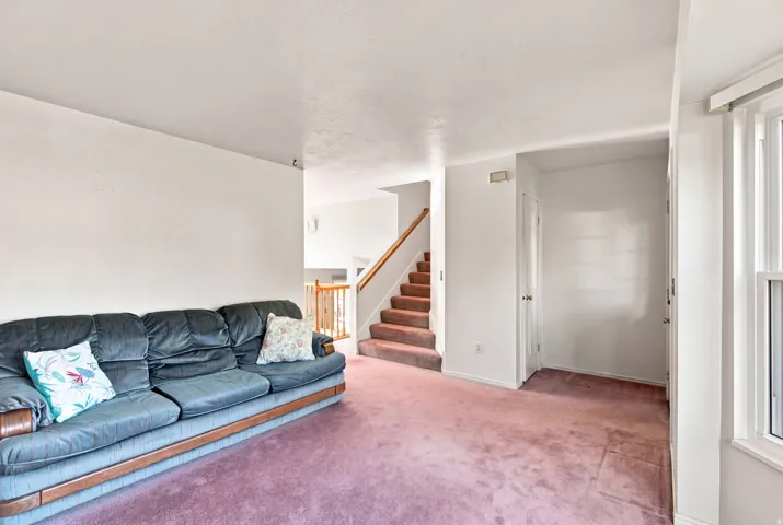 Staircase with wood handrail and neutral-toned risers, light-colored walls, and a window with white trim