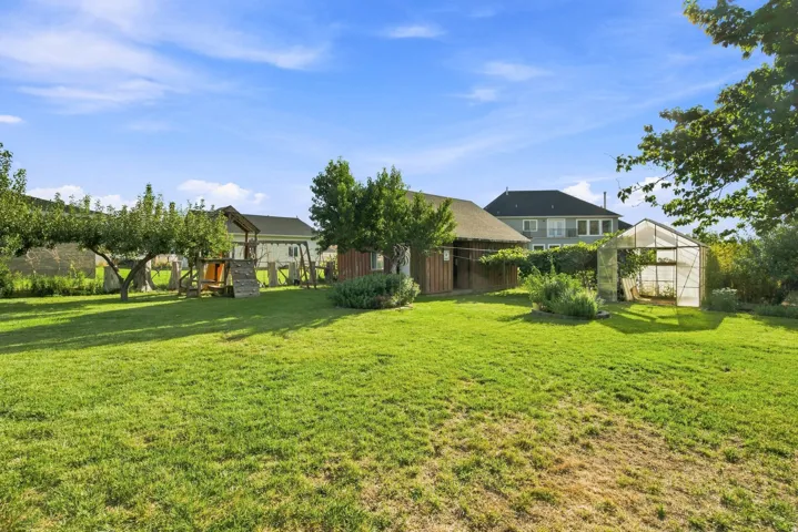 Expansive green lawn with mature trees and a greenhouse structure