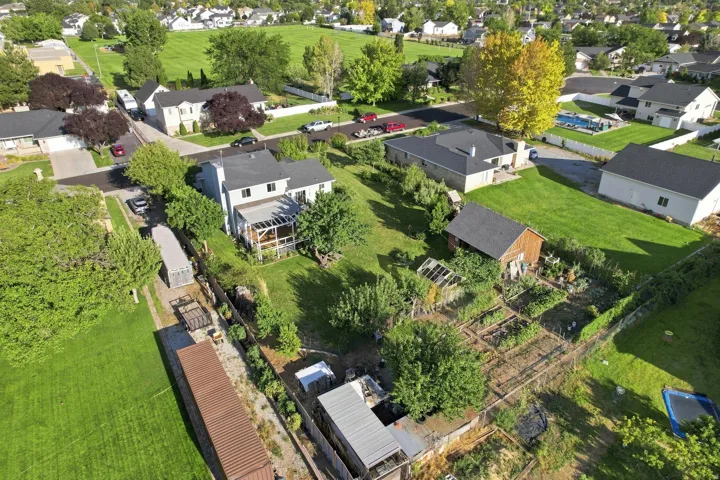 Expansive property featuring a two-story residence with a covered deck, a separate outbuilding, a greenhouse, and established garden plots