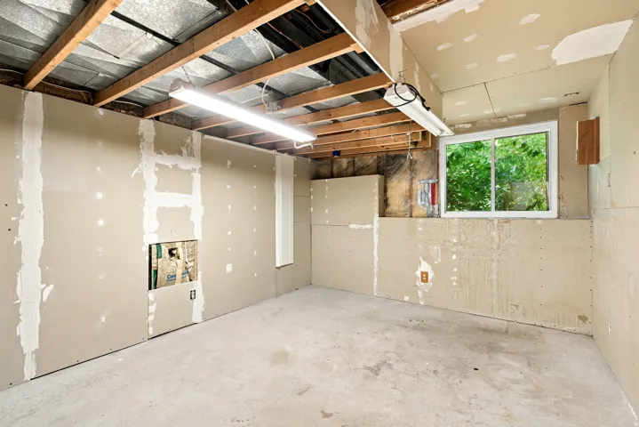 Unfinished interior space featuring exposed ceiling joists, partially installed drywall, concrete flooring, and a sliding window