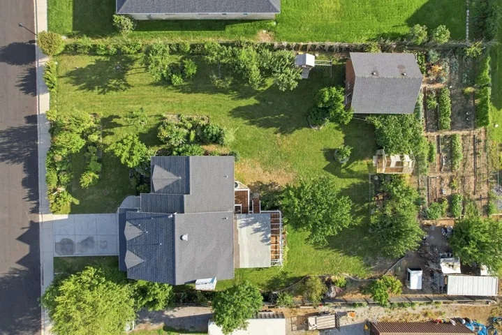 Aerial view of the property featuring a main residence, detached auxiliary structure, extensive landscaped grounds, and dedicated garden plots