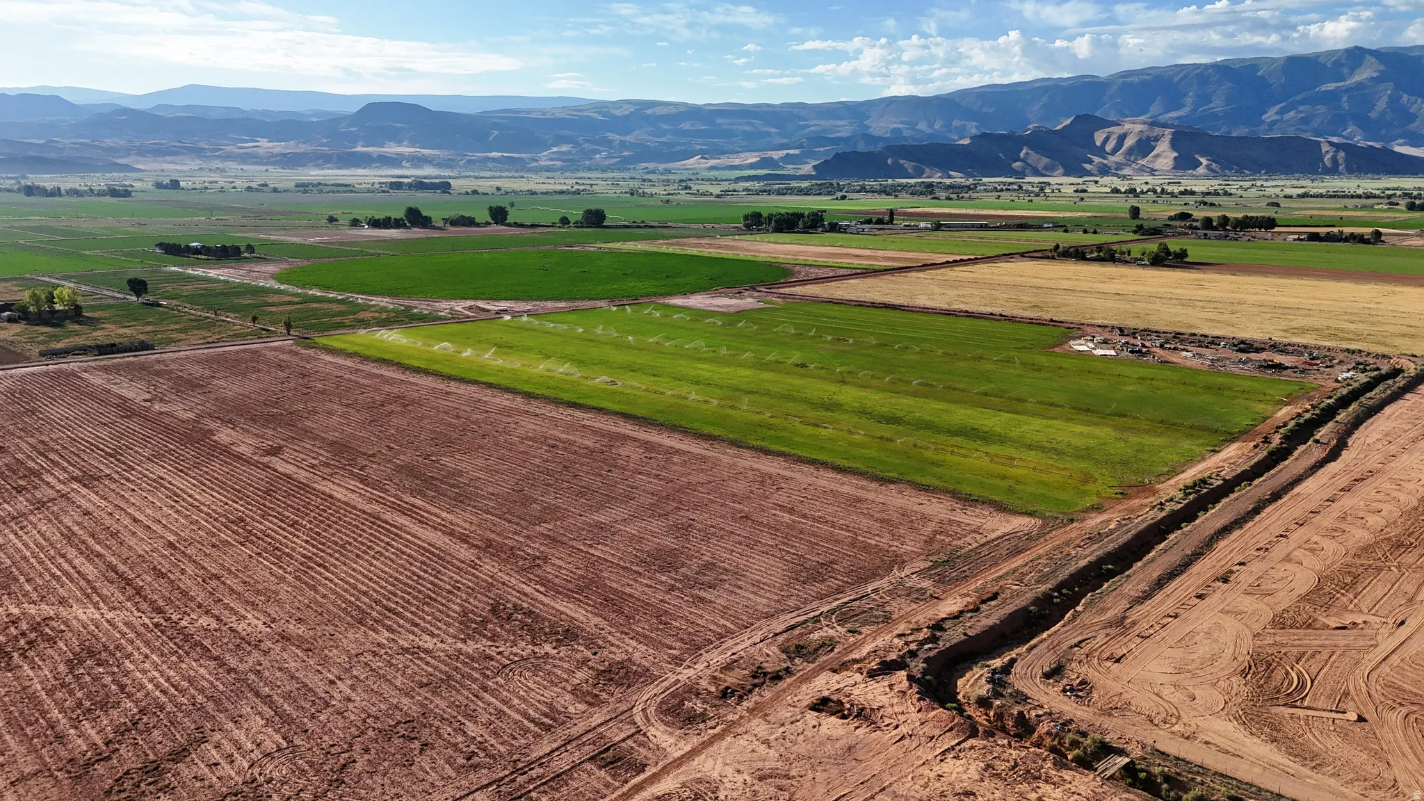 Expansive agricultural land featuring tilled fields, irrigated crops, and a mountainous backdrop