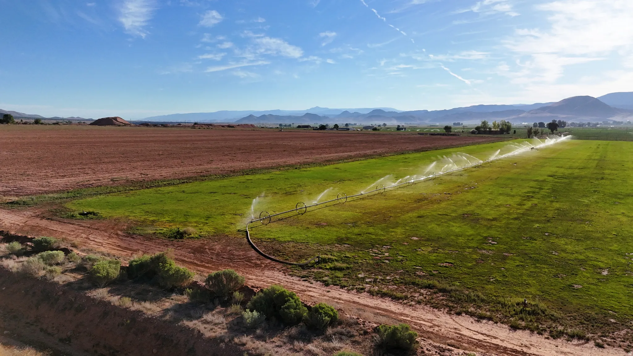 Expansive agricultural land featuring a center pivot irrigation system, cultivated fields, and distant mountain scenery