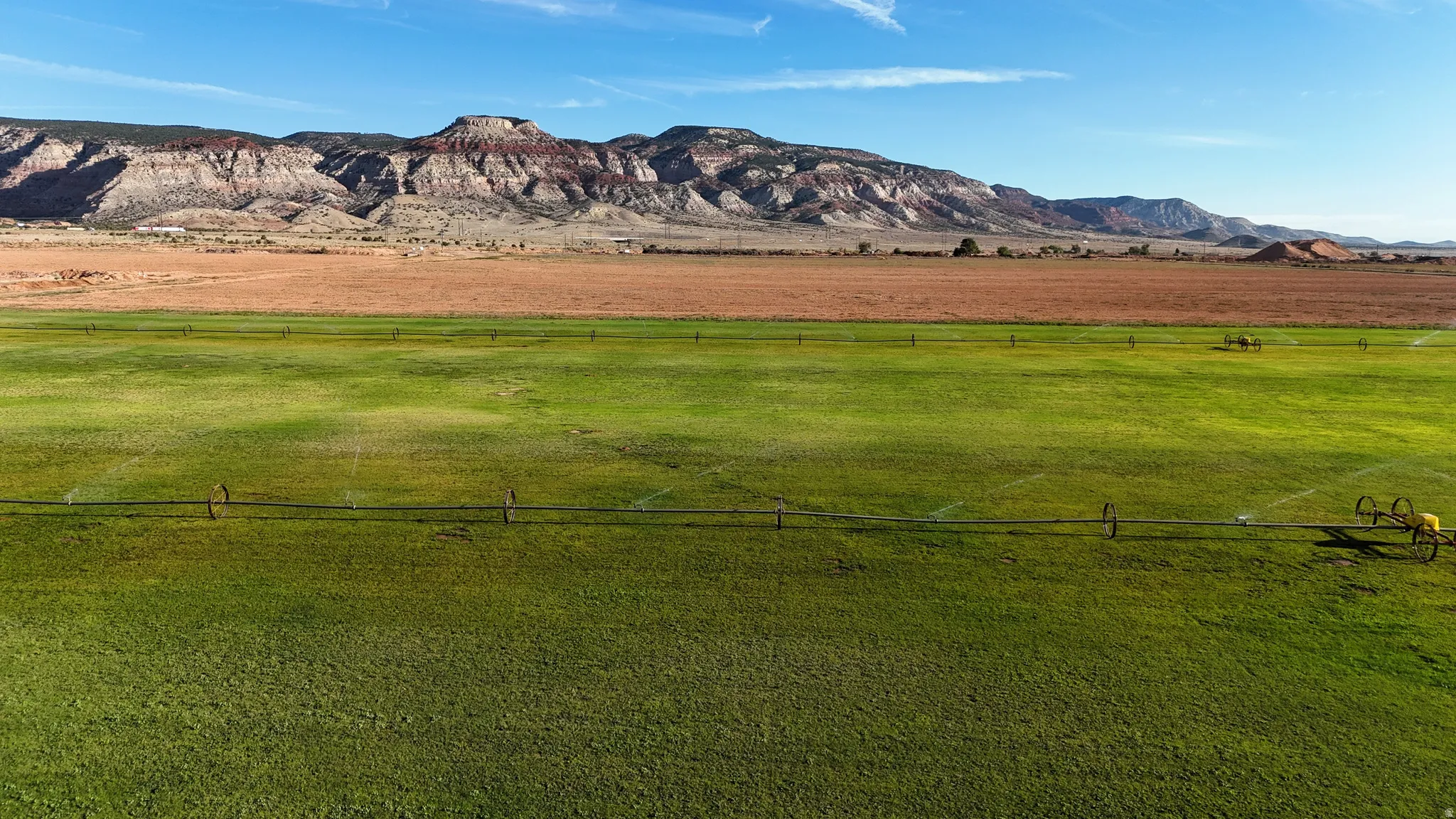 Expansive green fields with irrigation systems, complemented by distant mountains and a clear sky