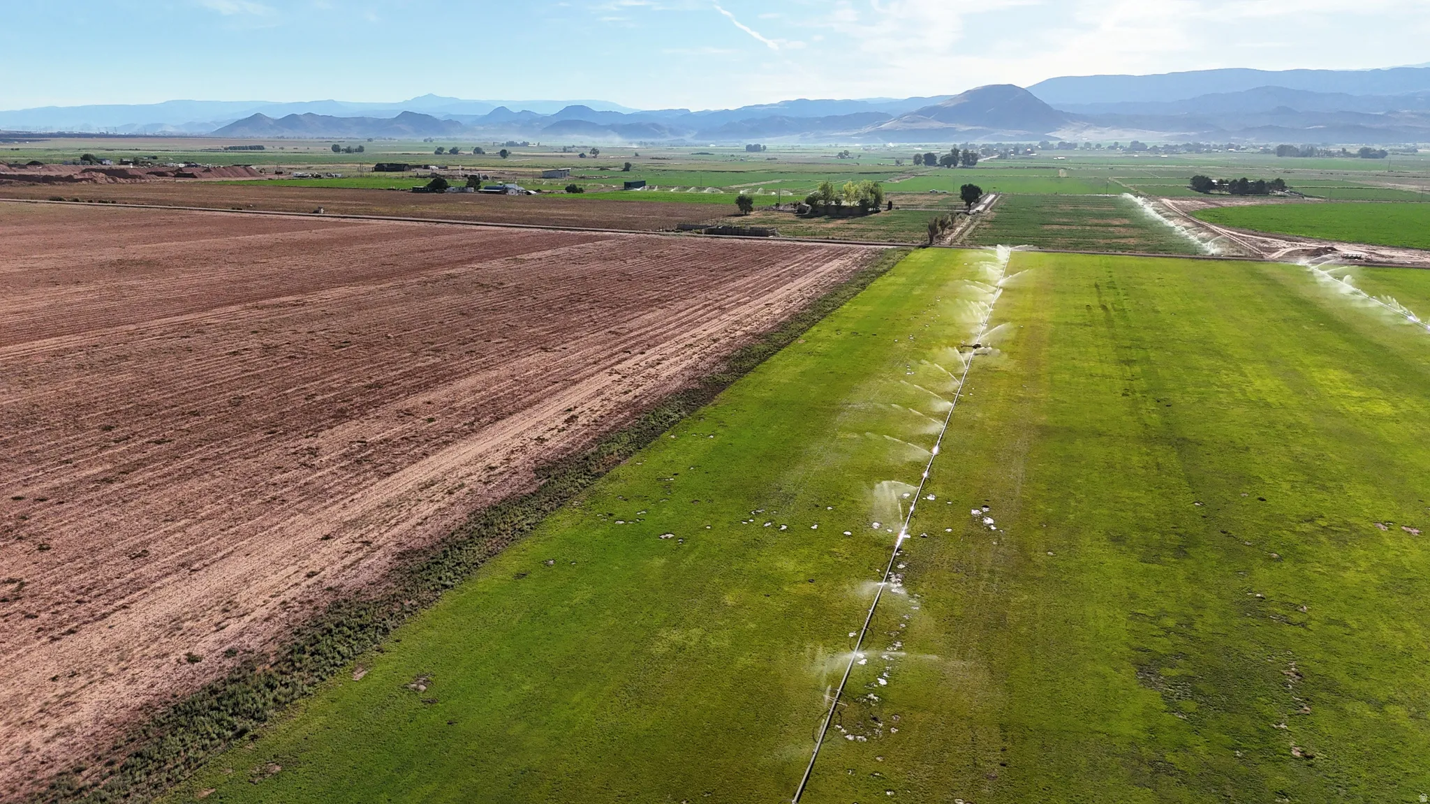 Expansive agricultural property featuring cultivated fields, active irrigation systems, and distant mountain ranges