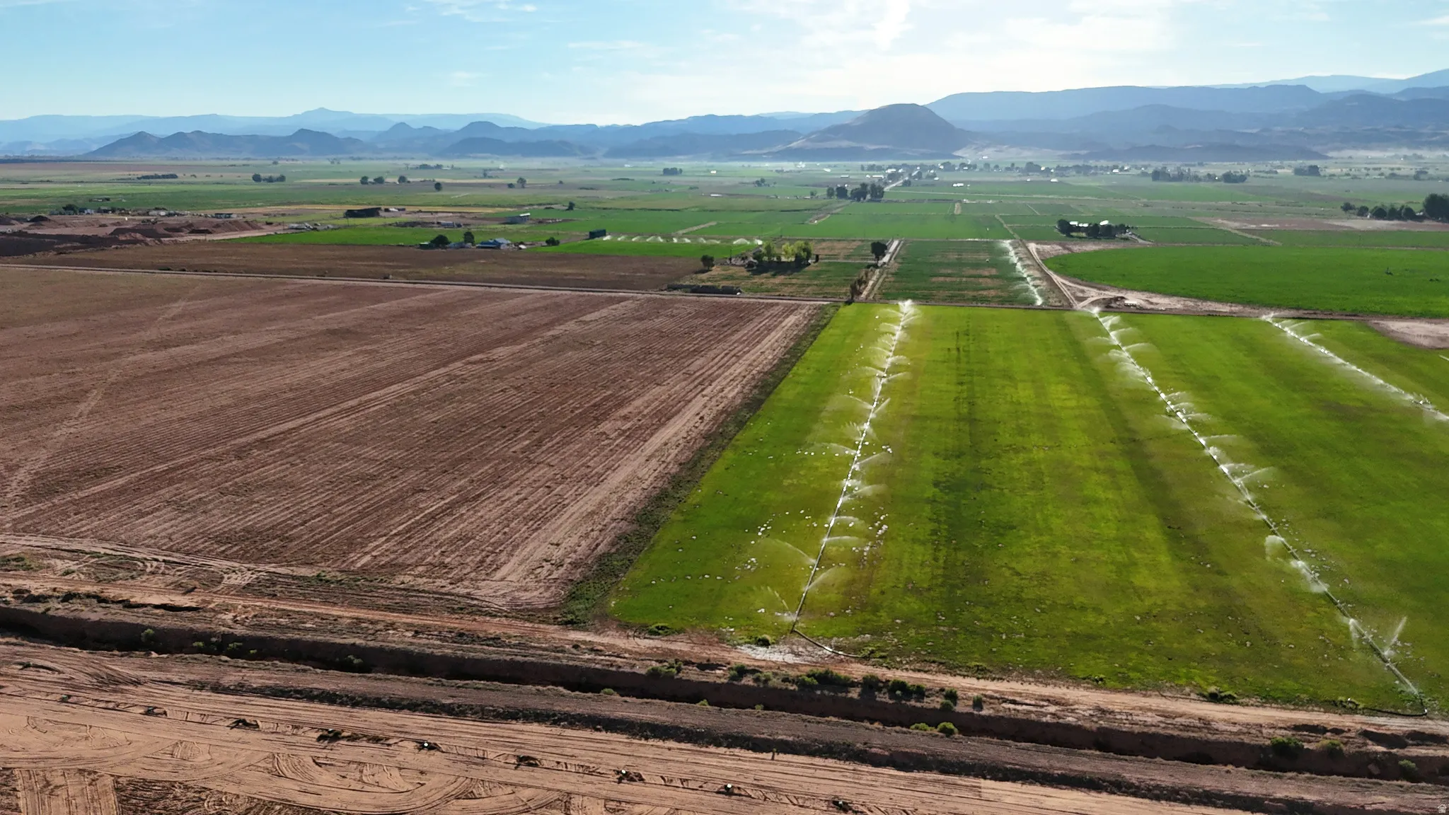 Expansive agricultural land featuring cultivated fields, green irrigated crops, and distant mountains