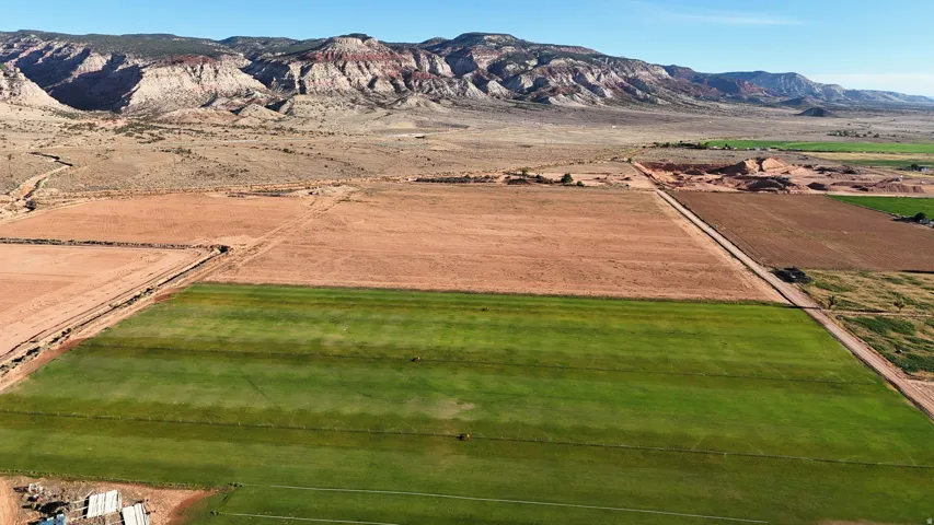 Expansive land parcel featuring cultivated green fields and arid terrain, bordered by distant mountainous formations