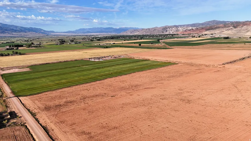 Expansive agricultural land featuring cultivated fields, a gravel road, and distant mountain ranges