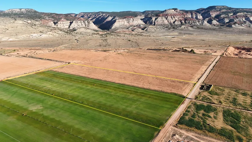 Expansive land parcel featuring cultivated fields, a defined dirt road, and prominent mountain backdrops