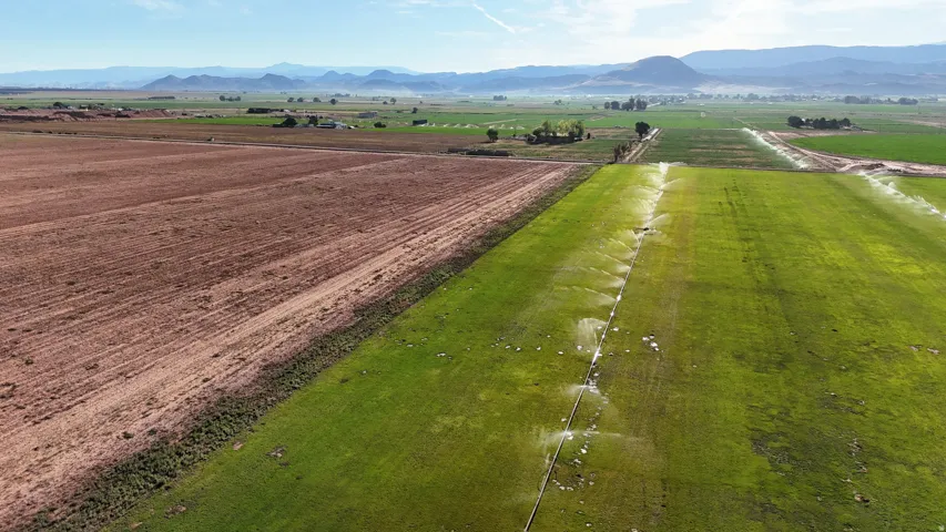Expansive agricultural property featuring cultivated fields, active irrigation systems, and distant mountain ranges