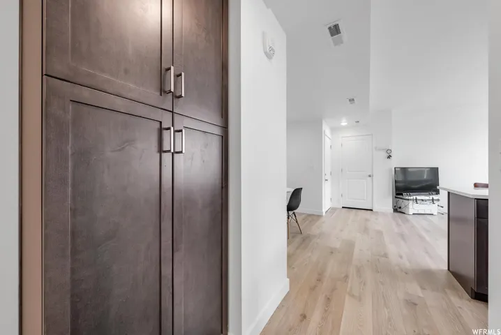 Full-height cabinetry with brushed metal pulls, light wood-finish flooring, white walls, and recessed lighting