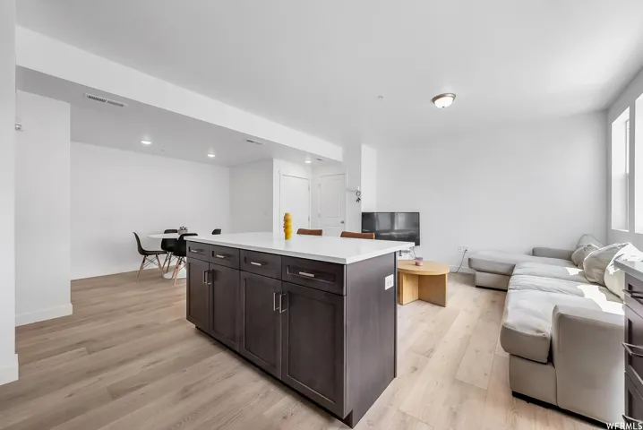 Open-concept living space featuring wood-finish flooring, recessed lighting, a kitchen island with storage and a light-toned countertop, and multiple windows