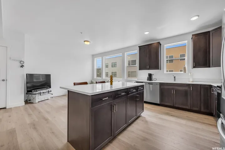 Open-concept living space with light wood-finish flooring, recessed lighting, and a kitchen island featuring dark wood cabinetry