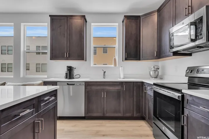 Kitchen featuring dark wood-finish cabinetry, light countertops, stainless steel appliances, and wood-finish flooring