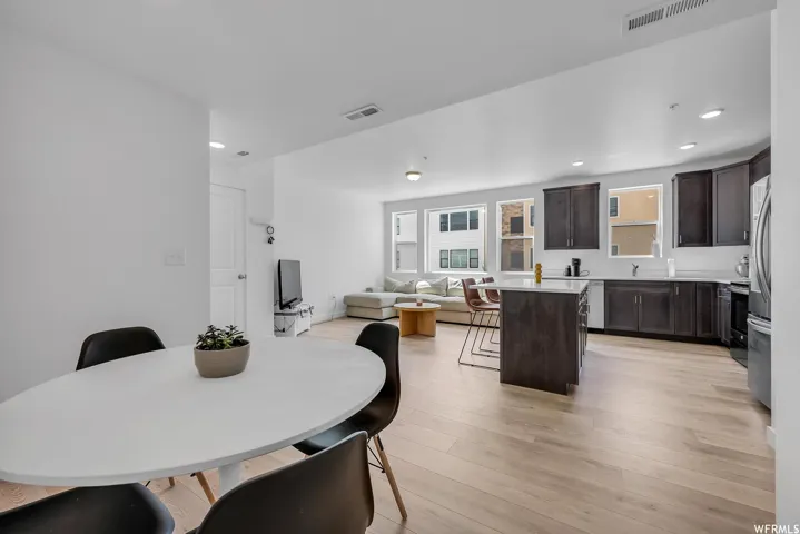 Open-concept living space featuring wood-finish flooring, recessed lighting, and a kitchen with dark cabinetry and a center island with seating