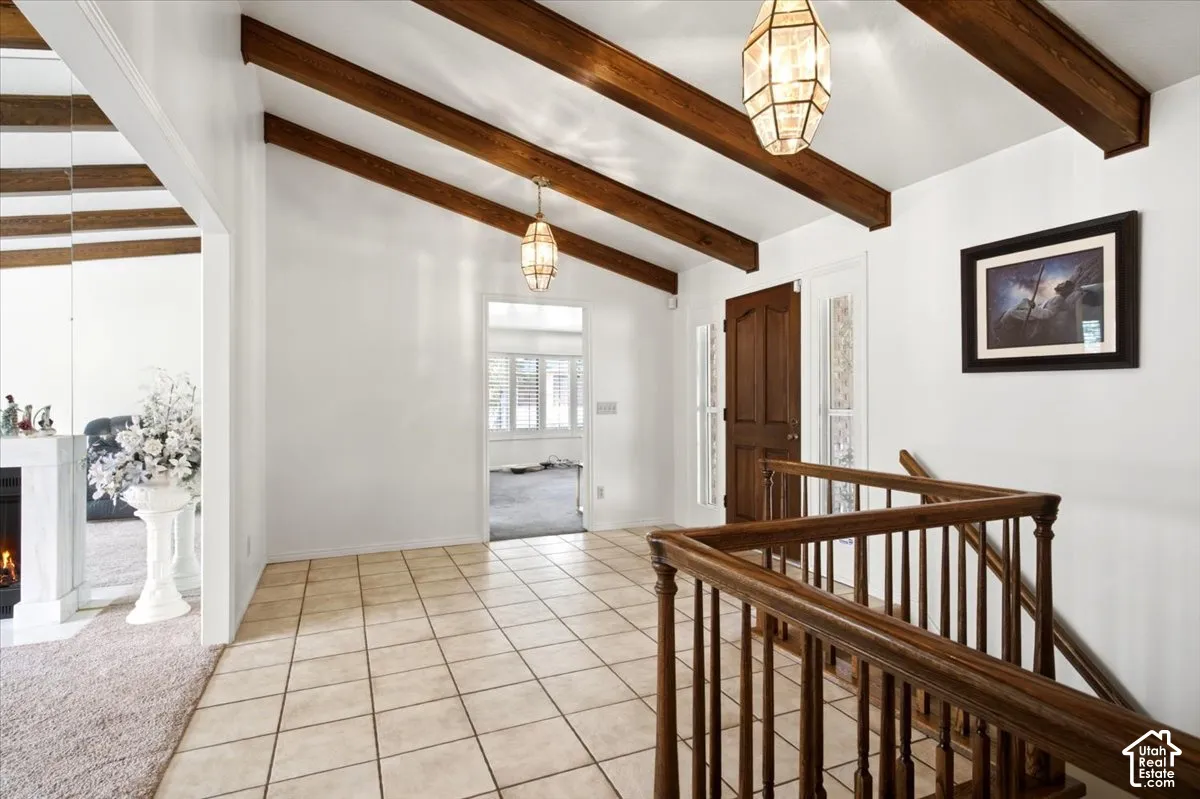 Vaulted ceilings with exposed wood beams, tile flooring, and a wood entry door with textured glass side panels