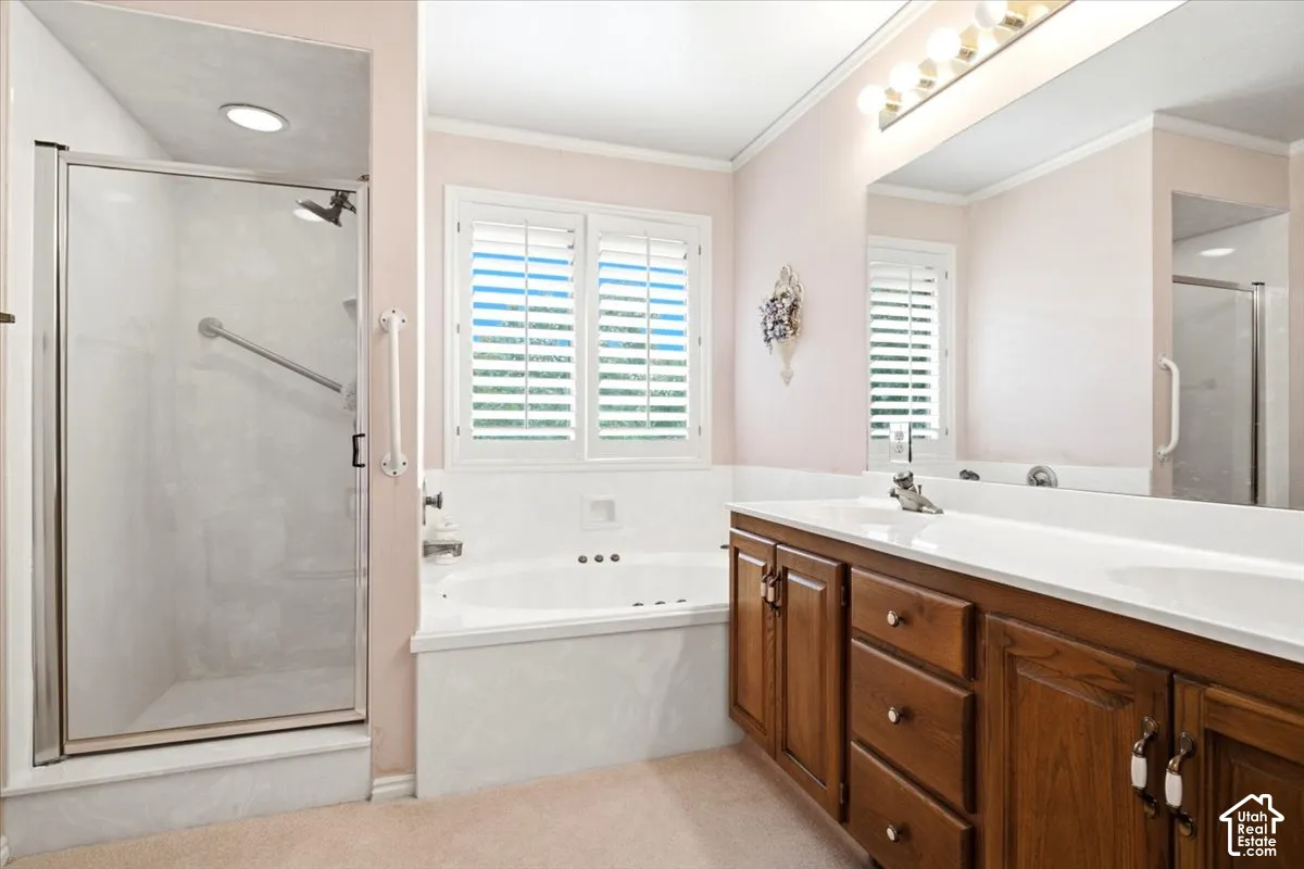 Dual vanity with integrated sinks, wood-finish cabinetry, built-in soaking tub, glass-enclosed shower, and window with plantation shutters