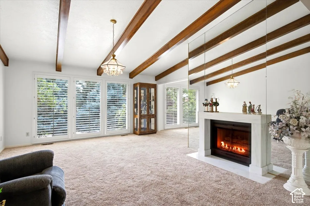 Vaulted ceiling with exposed wood beams, three large windows with plantation shutters, fireplace with a white surround and hearth, and a built-in display cabinet