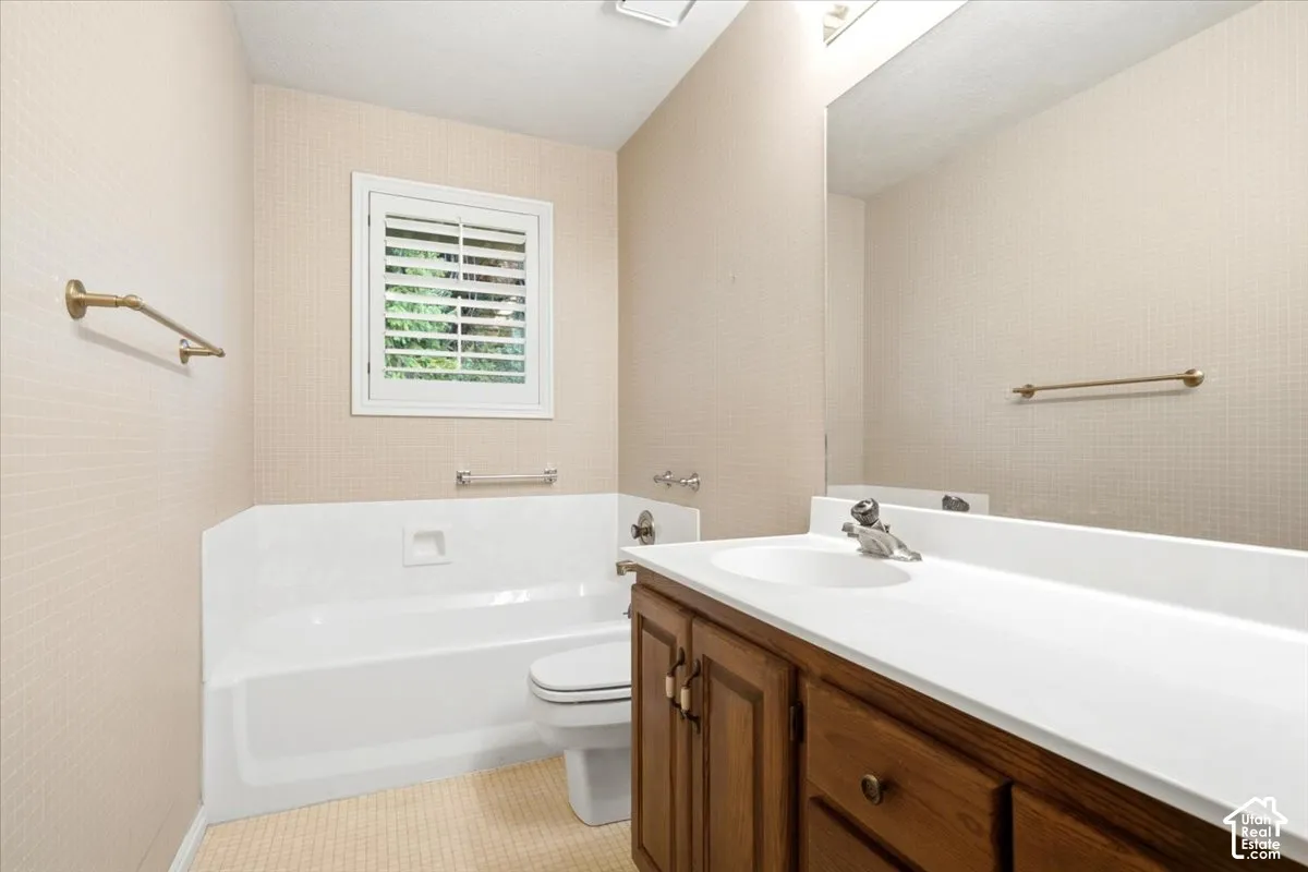 Bathroom featuring a single vanity with wood cabinetry, a white countertop, an integrated sink, a built-in bathtub, and a window with white plantation shutters