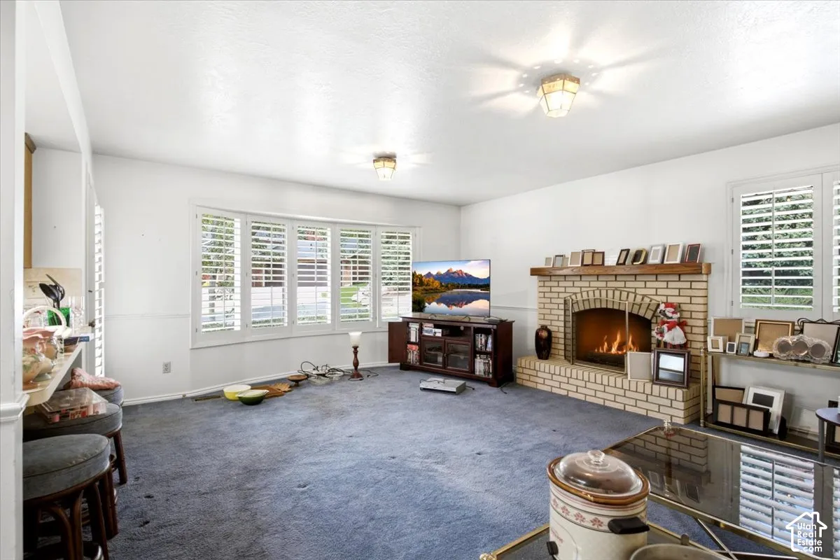 Living area featuring a brick fireplace with wood mantel, bay window with plantation shutters, and two ceiling-mounted light fixtures