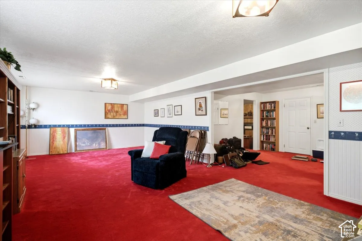 Spacious recreation room featuring vibrant red wall-to-wall carpeting, decorative tile wainscoting in navy and white, recessed ceiling lighting, and multiple doorways providing access to adjoining spaces