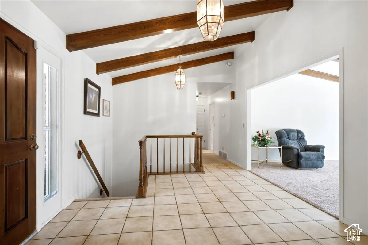 Vaulted ceiling with exposed wood beams, tile flooring, wood-paneled entry door, sidelight window, and a wood banister