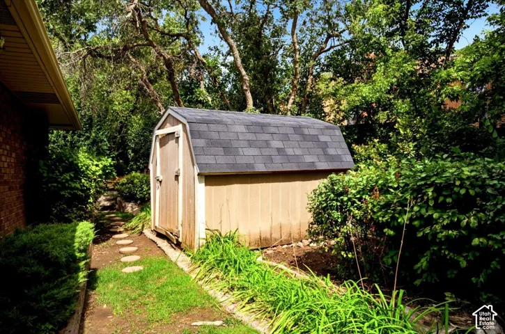 Detached storage shed with shingle roof, stone-paver walkway, and lush landscaping