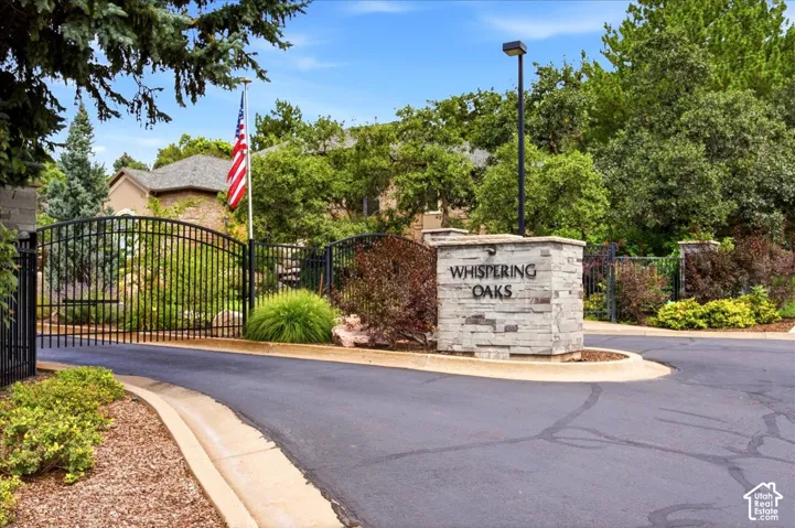 Gated community entrance featuring stacked stone signage, wrought iron fencing, and mature landscaping