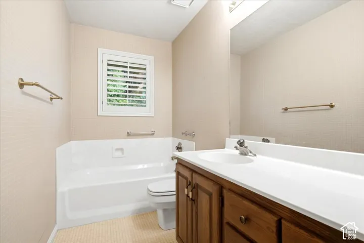 Bathroom featuring a single vanity with wood cabinetry, a white countertop, an integrated sink, a built-in bathtub, and a window with white plantation shutters