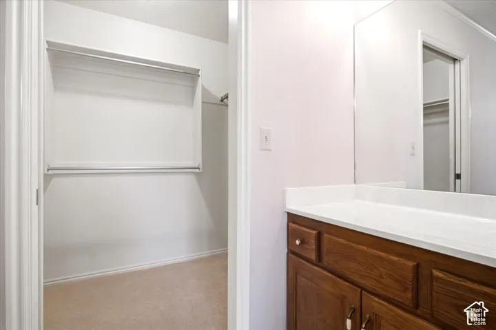 Built-in closet with dual hanging rods, wood-finish vanity with white countertop, and wall-mounted mirror